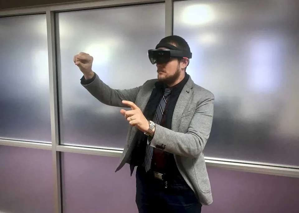 A researcher wearing an augmented-reality headset and gesturing at a hologram.