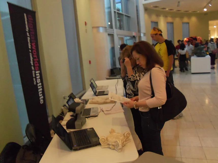 Visitors at demonstration tables with laptops and plaster casts beside a Digital Worlds Institute banner.