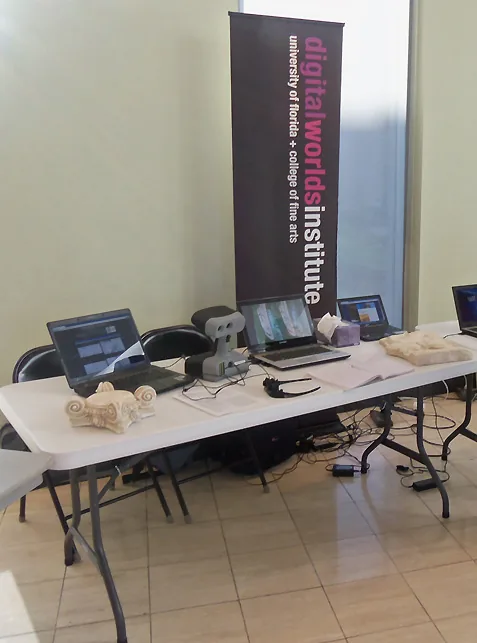An exhibit table with laptops and plaster casts next to a Digital Worlds Institute banner.