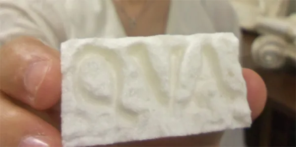 Close-up of a hand holding a 3D-printed block with the raised letters QVA.