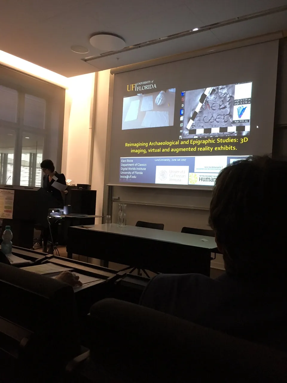 Audience view of a projection screen showing a slide about 3D imaging and virtual and augmented reality for archaeology.