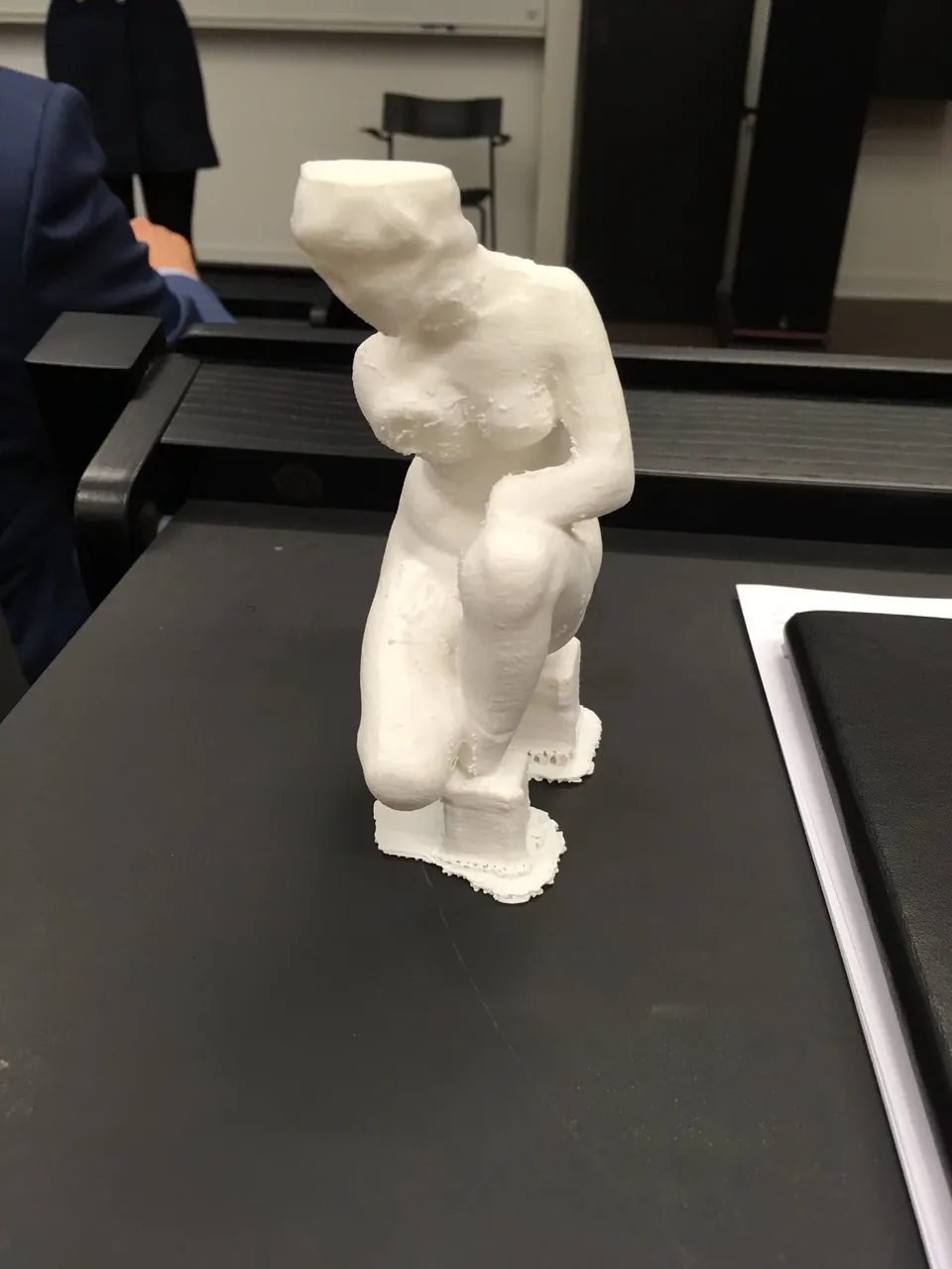 A small white 3D-printed statuette of a crouching figure on a table.