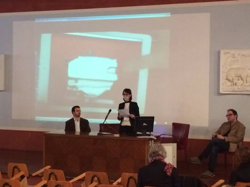 Speakers seated at a panel table in front of a projected 3D-shaded image.