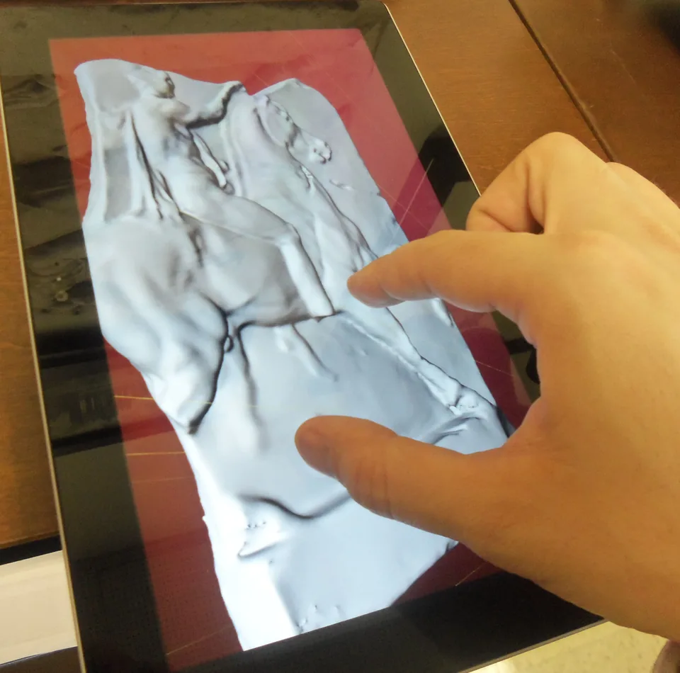 A hand touching a tablet that displays a blue-tinted 3D relief model.